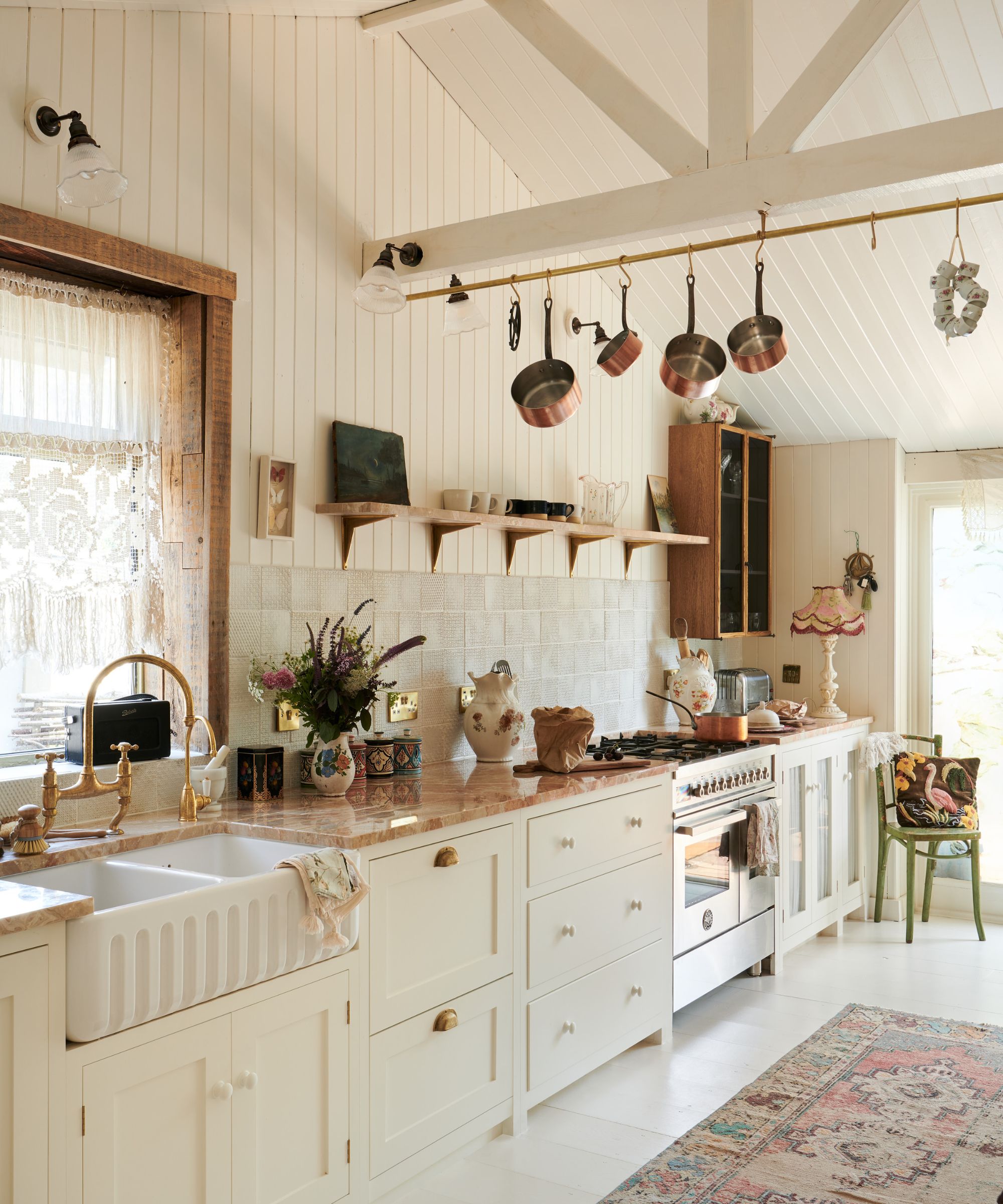 A single-wall farmhouse kitchen with white cabinets, white shiplap paneling on the walls, and copper pots hanging from the ceiling beams