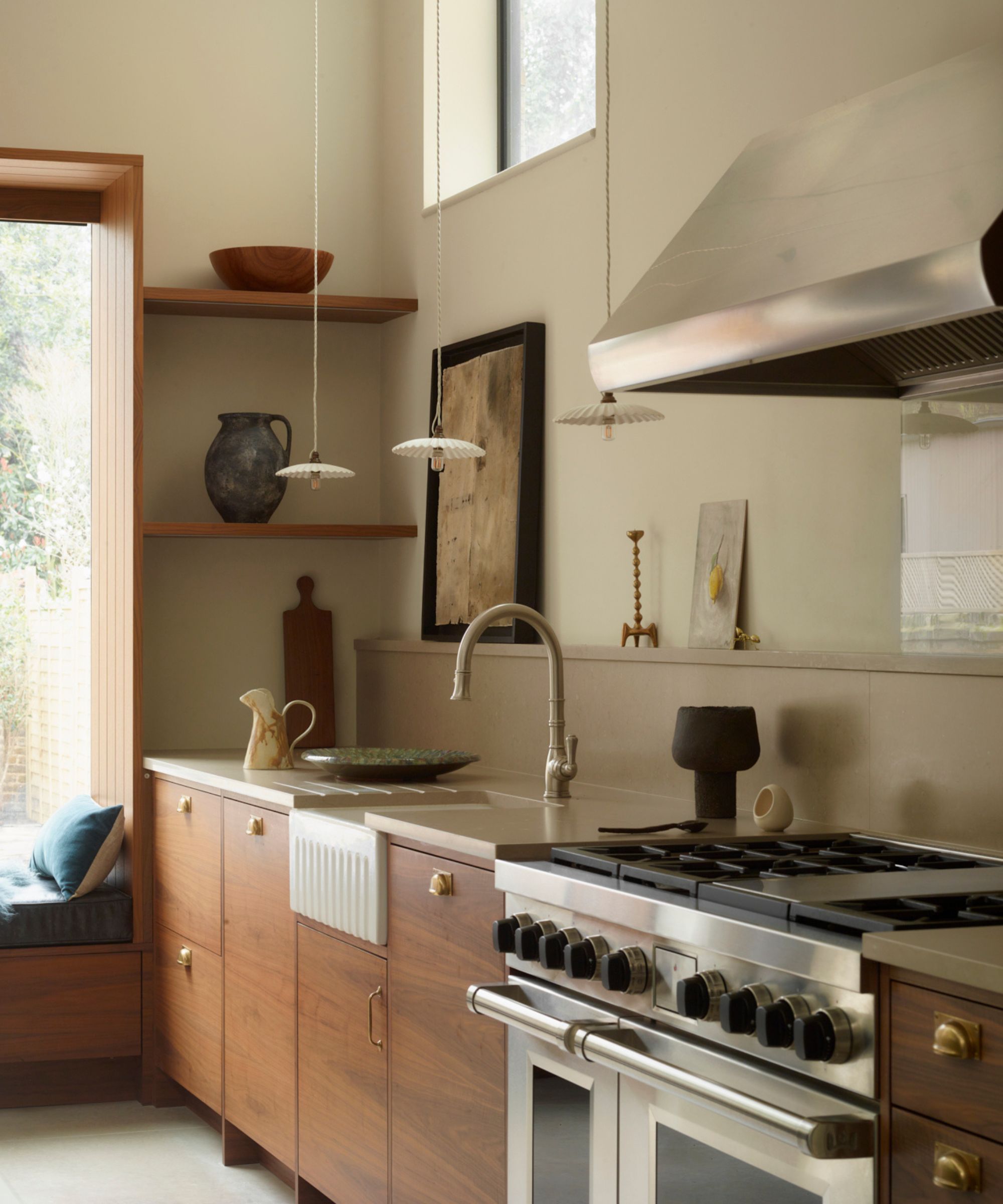 A single-wall kitchen with wood cabinets, stainless steel appliances, white walls, and open shelving with artwork