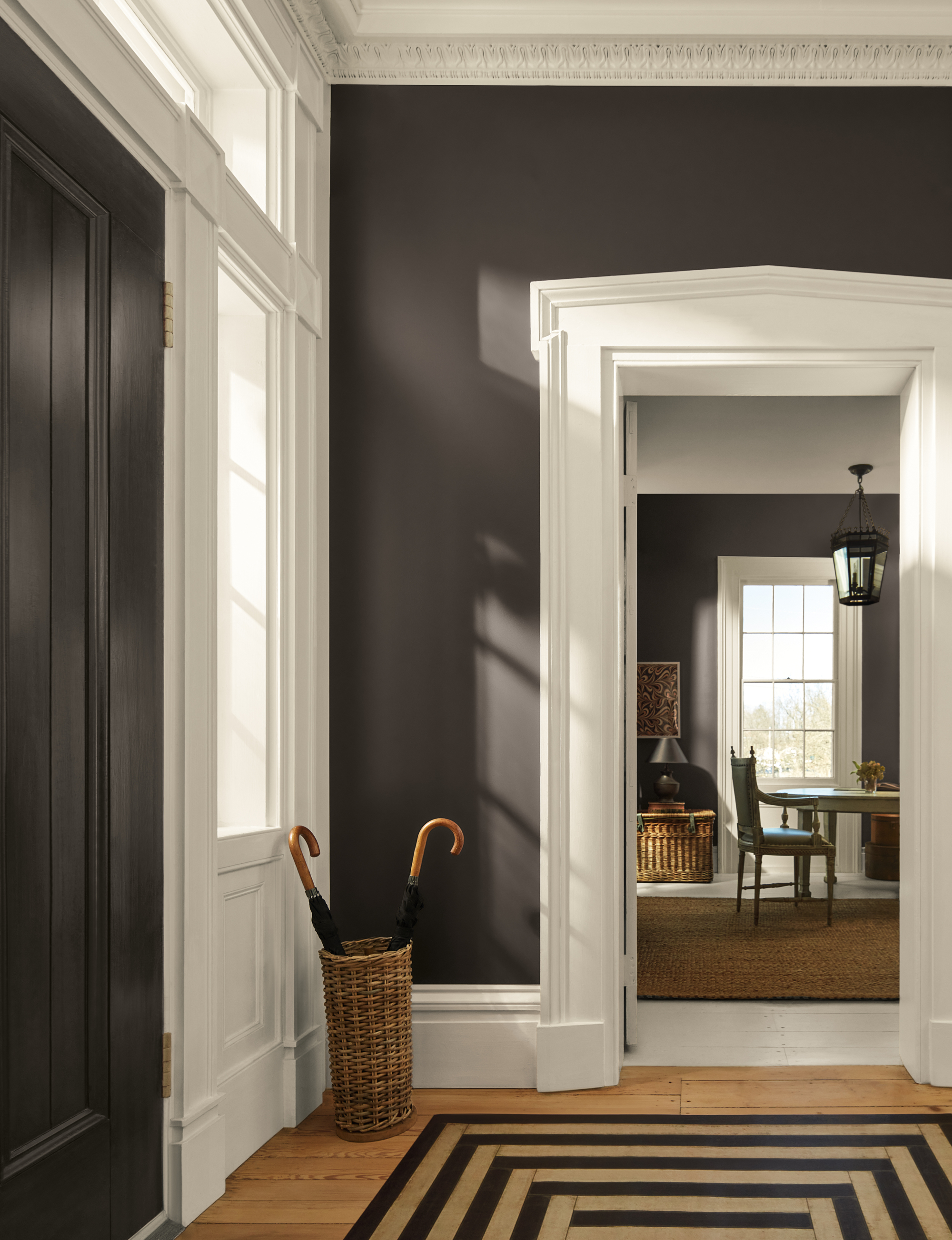 An entryway painted in a dark gray-brown color with thick white trim and a woven umbrella basket