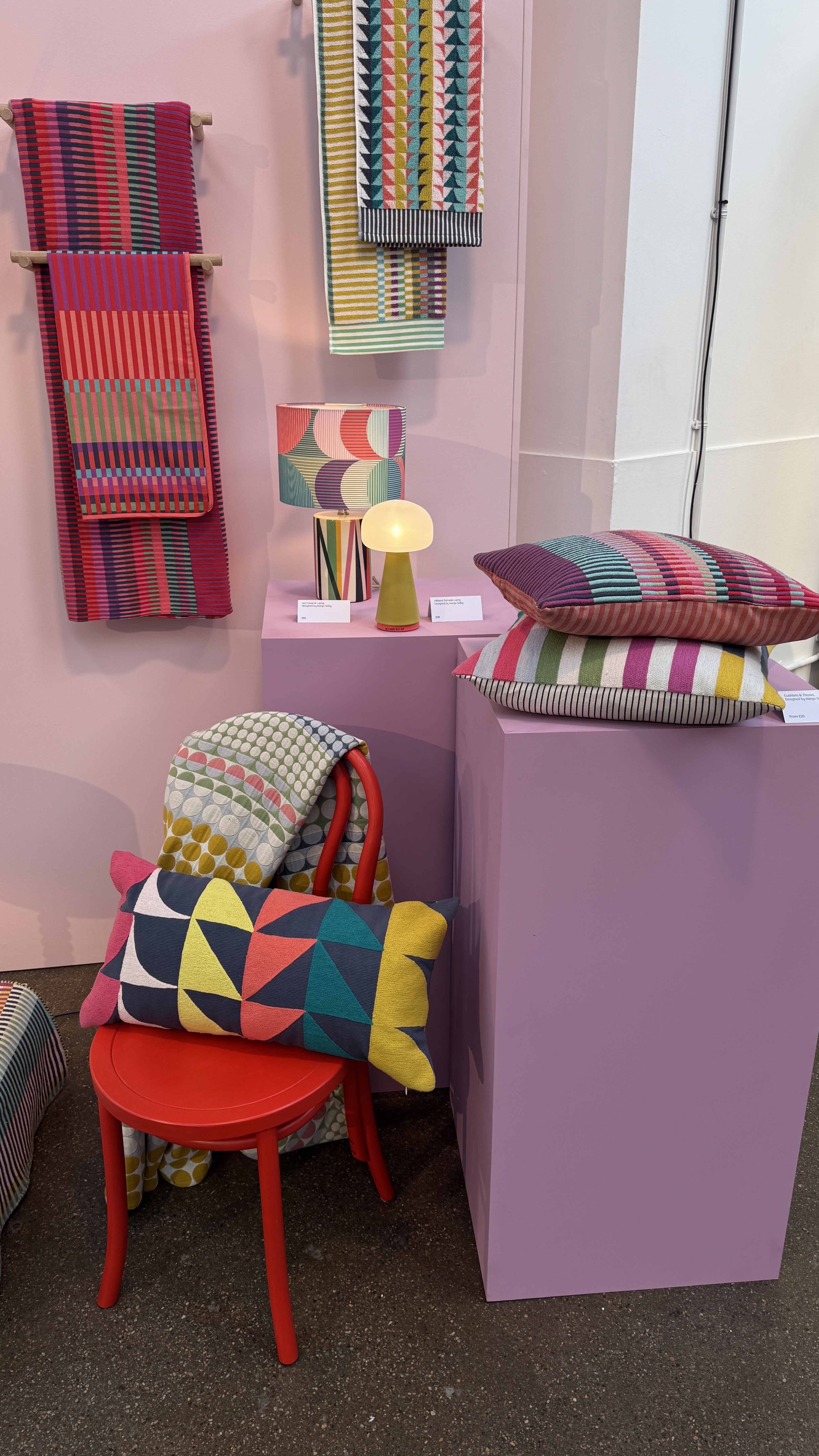 Colorful pillows and towels on a pink wall and a pink base and a red chair
