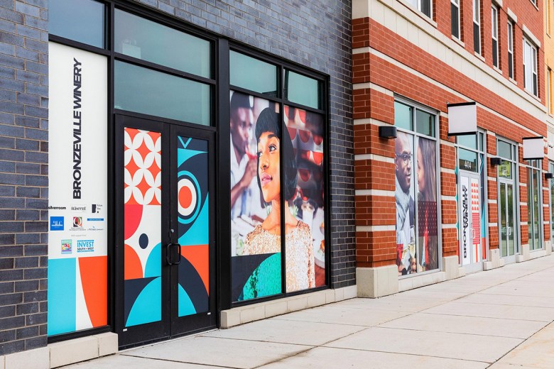 The facade of Bronzeville Winery, a dark brick building, features a series of color photographs of Black people alongside the name in white, white, bold black text and geometric patterns in orange, light blue and navy blue.