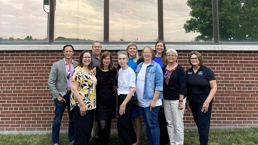The Department of Campus Planning and Architecture, a group of 10 Purdue faculty and fellows, stand together in front of a brick building and smile at the camera.