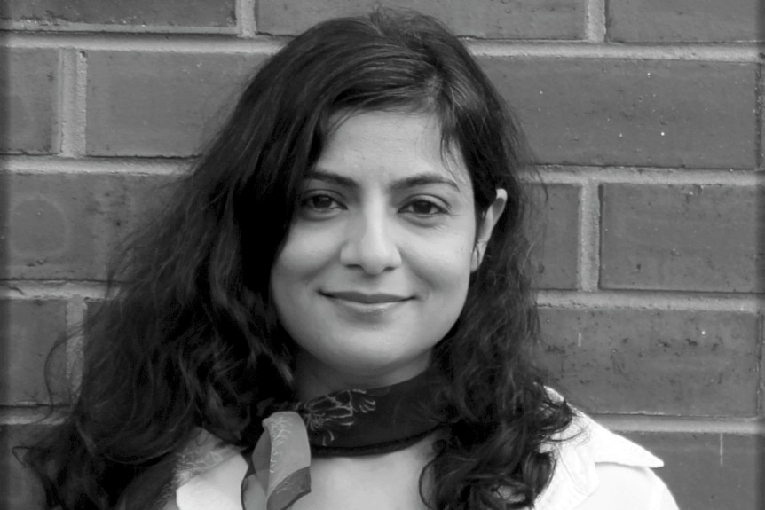 Black and white photo of a woman smiling at the camera wearing a white shirt and a dark banana around her neck