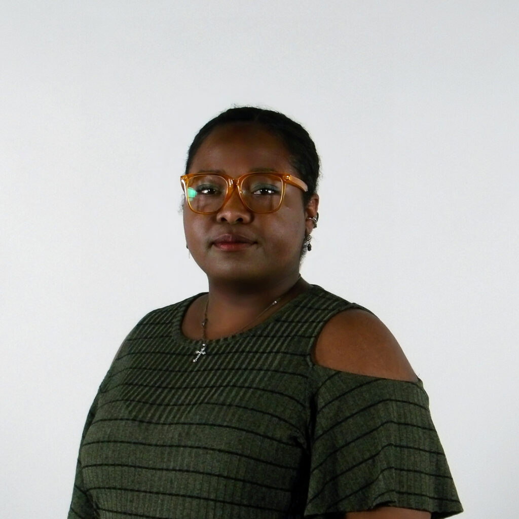 A person wearing glasses and a green top with cut-out shoulders against a white background.