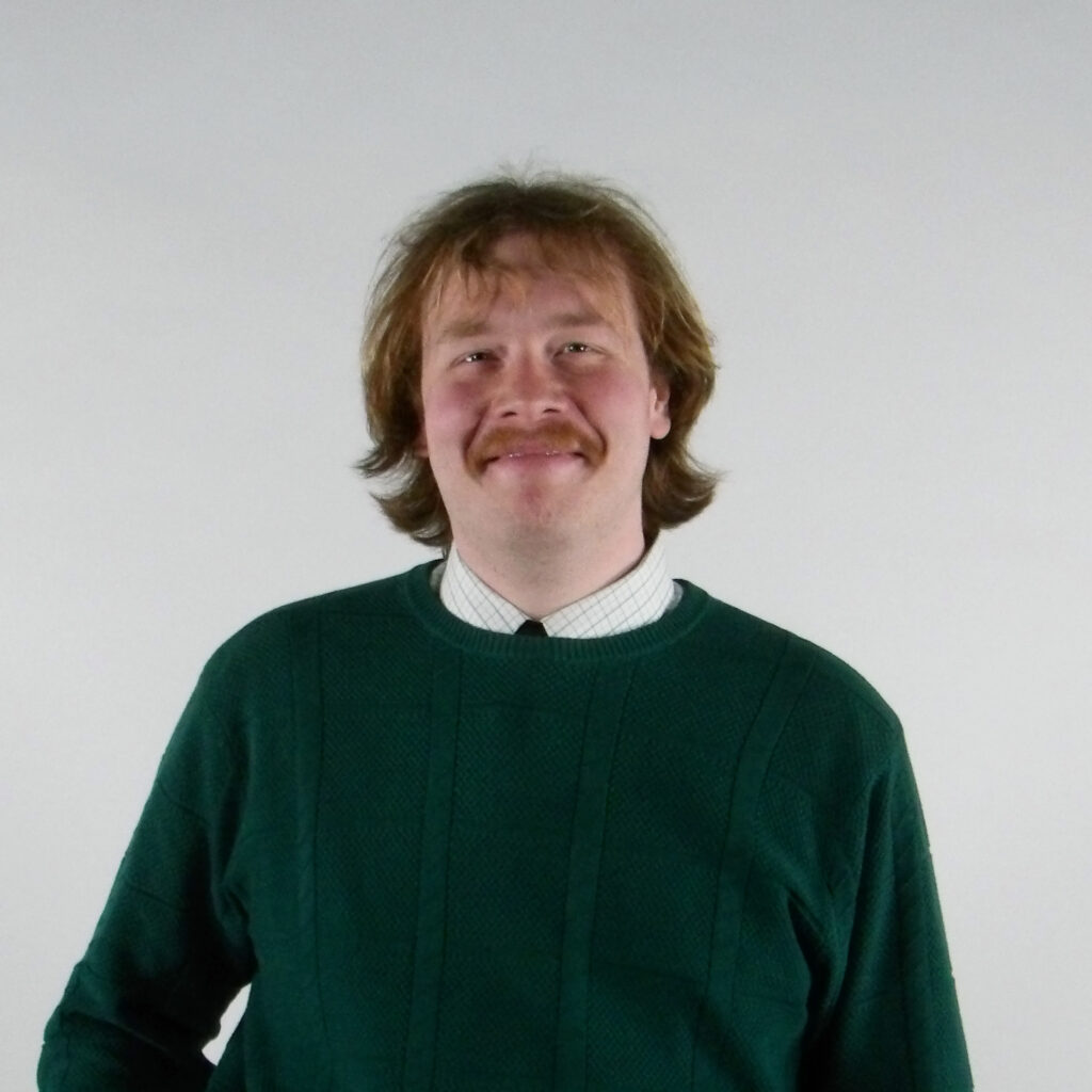 Smiling person in a green sweater with a white collared shirt underneath.