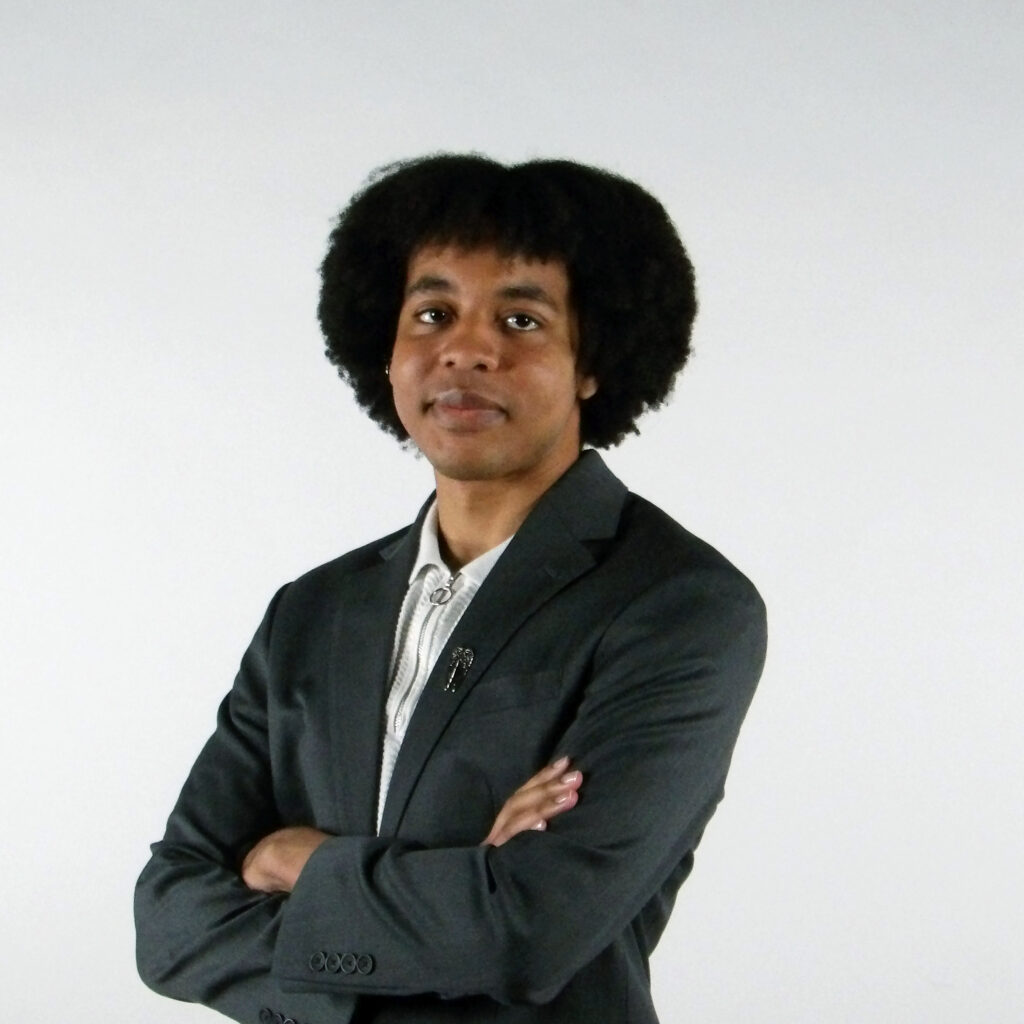 Person with Afro hairstyle in dark suit, arms crossed.