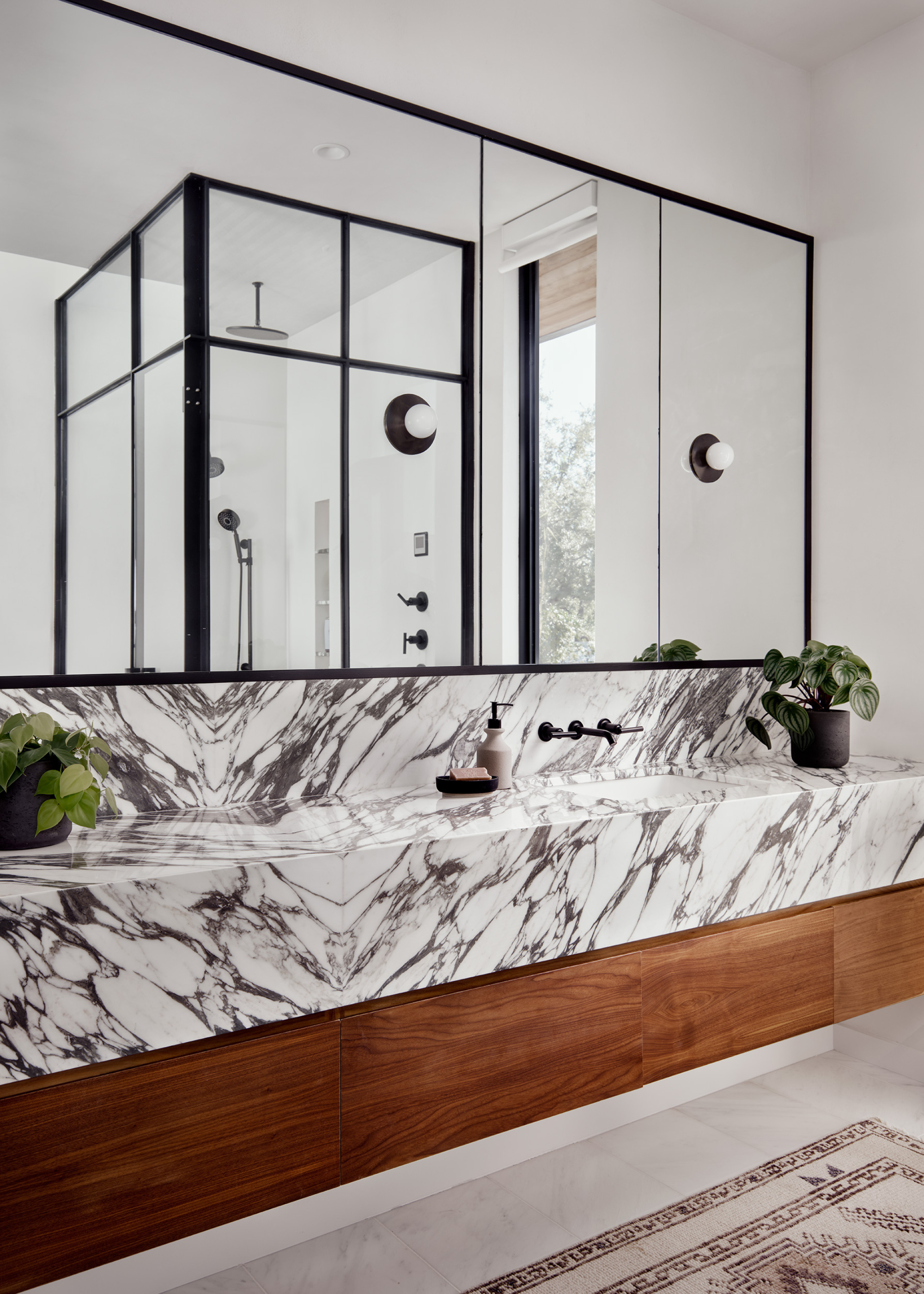 A white bathroom with mirror cabinets, marble counters and a few potted plants
