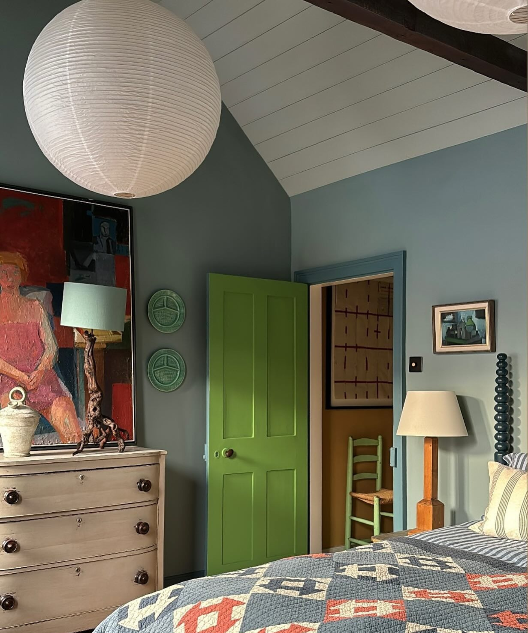 a bedroom with a quilt on the bed, a white dresser, blue painted walls and a green door