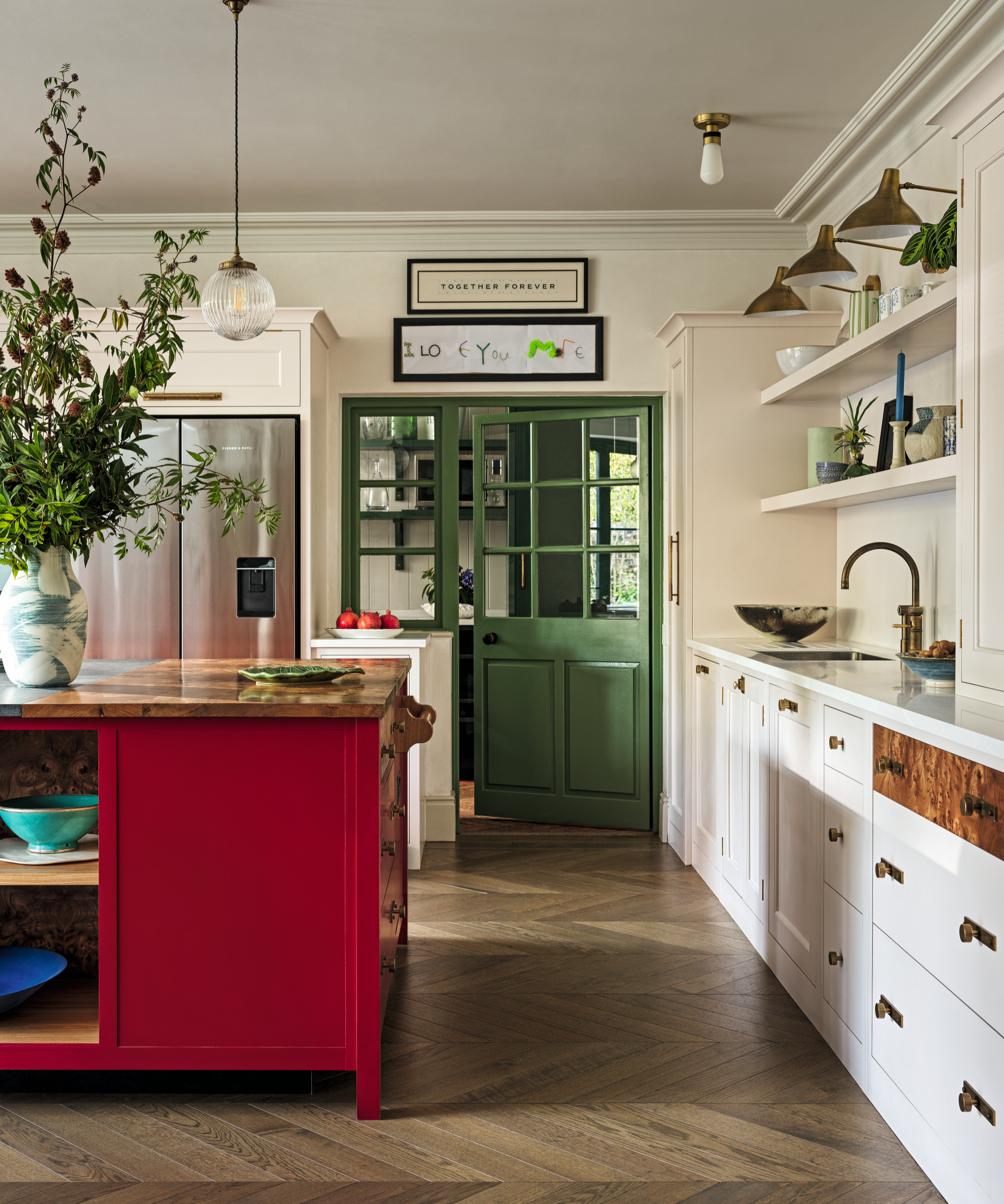 a kitchen with a red island, white cabinets, open shelving and a green pantry door
