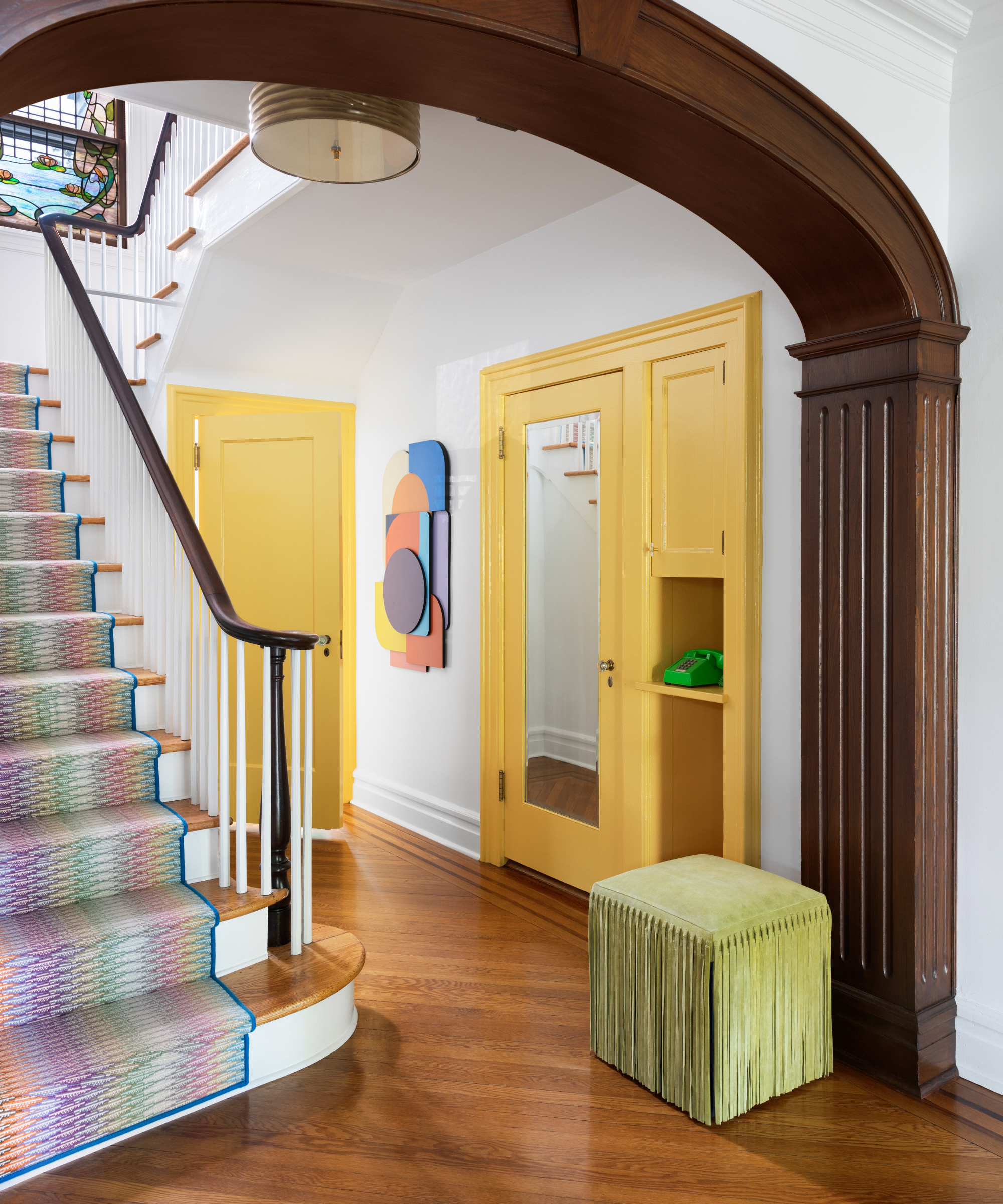 an entryway with a staircase with a colorful stair runner rug, a green ottoman and two yellow accent doors