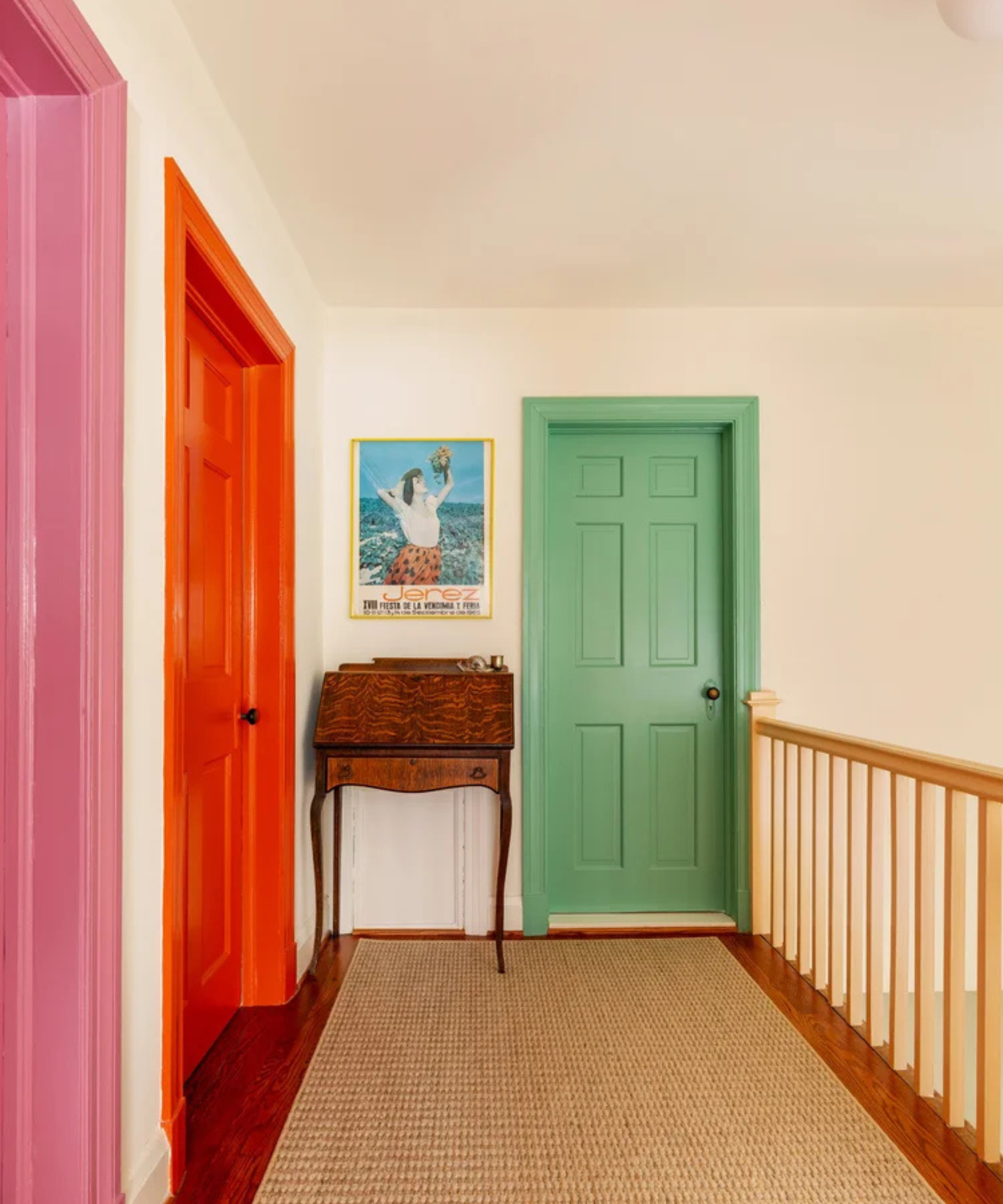 a hallway with three doors in pink, orange and green and a jute rug on the floor