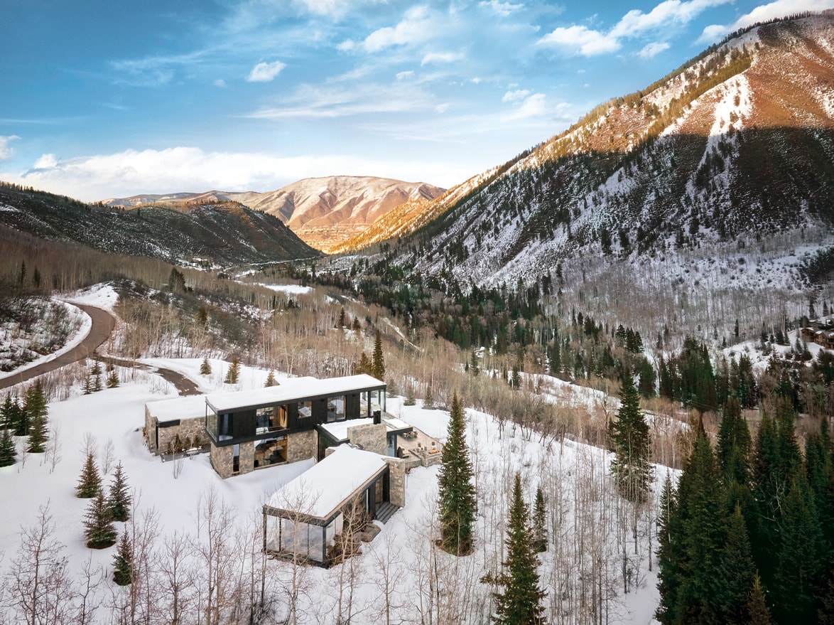 Modern house in snowy mountain landscape with clear blue sky and sunlit peaks in the background