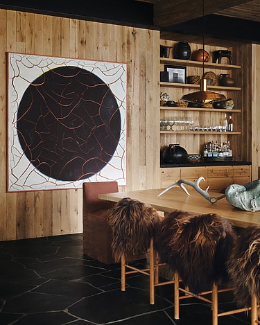 Cozy wooden dining room with a large abstract mural and fur-covered chairs around a wooden table.