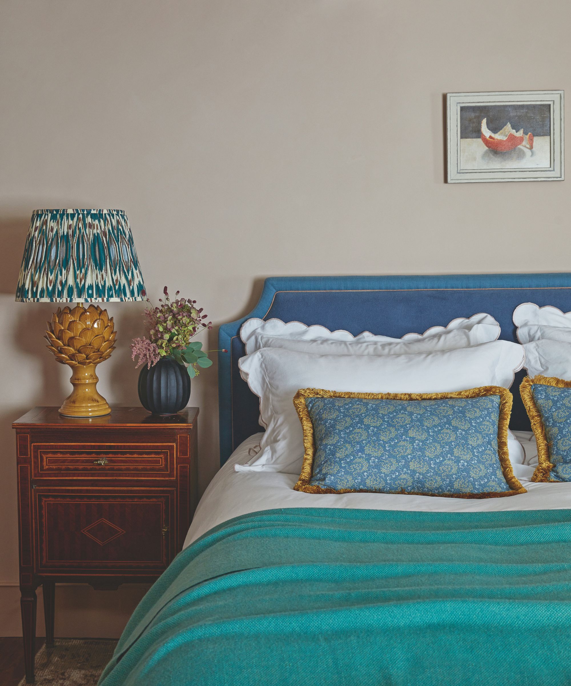 Bedroom with warm beige walls and bed with blue headboard and turquoise throw and a wooden bedside table
