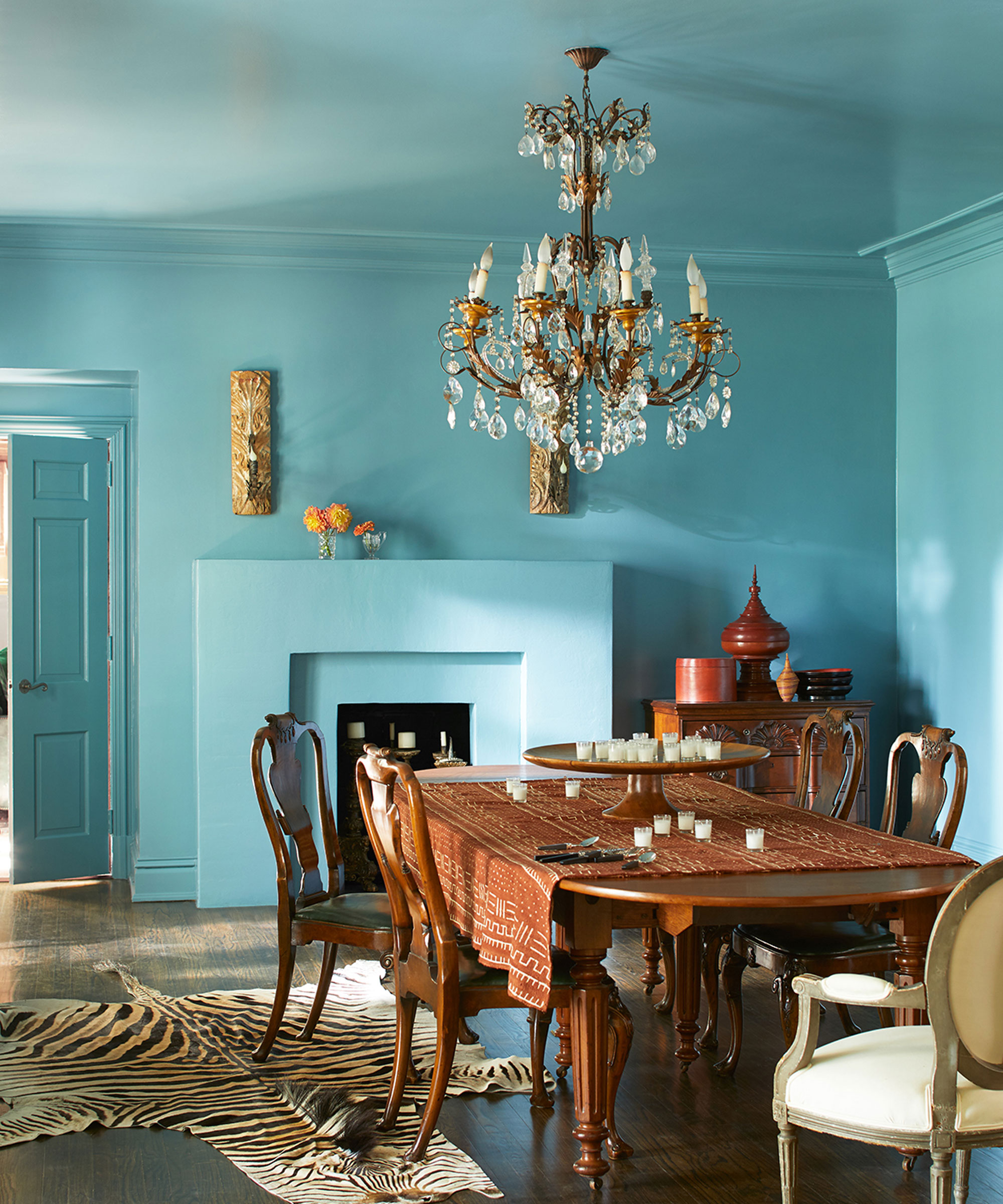 Turquoise painted dining room with dark wooden furniture, chandelier, animal print rug and wooden floor