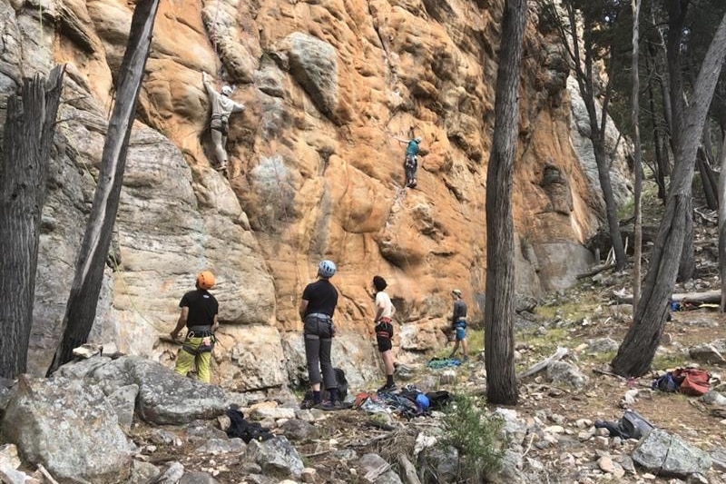 Four climbers are belaying themselves while two are on the rock face. everyone wears colorful helmets.