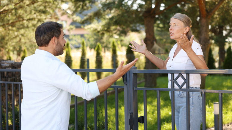 A male and female neighbor argue over a fence that separates their property.