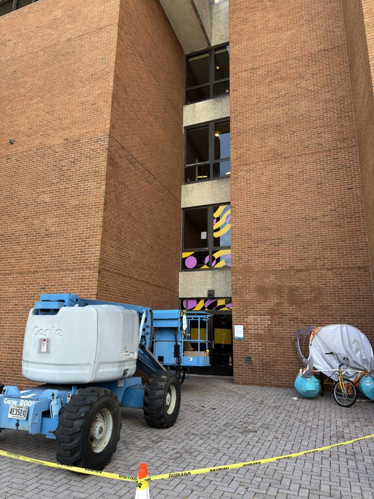 Brick building (fine arts) with colorful abstract window designs and a nearby pole with an art banner.