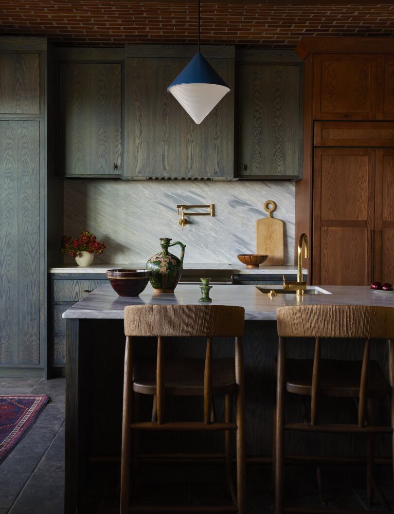 A modern kitchen with dark wooden cabinets, a marble backsplash, an island with two wooden chairs and a blue and white pendant light on the ceiling.