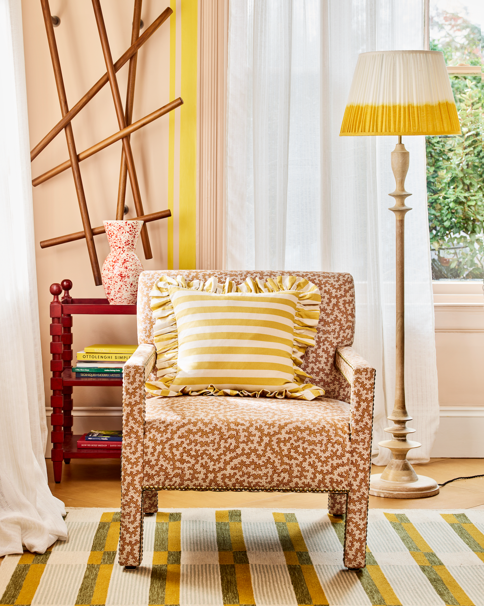 a living room with a patterned armchair, a red side table and a white curtain