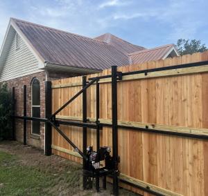 Automatic driveway gate attached to a wooden privacy fence on a home in Louisiana.