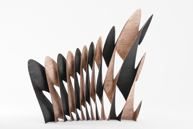 Modern abstract sculpture with alternating black and copper curved panels on a white background.