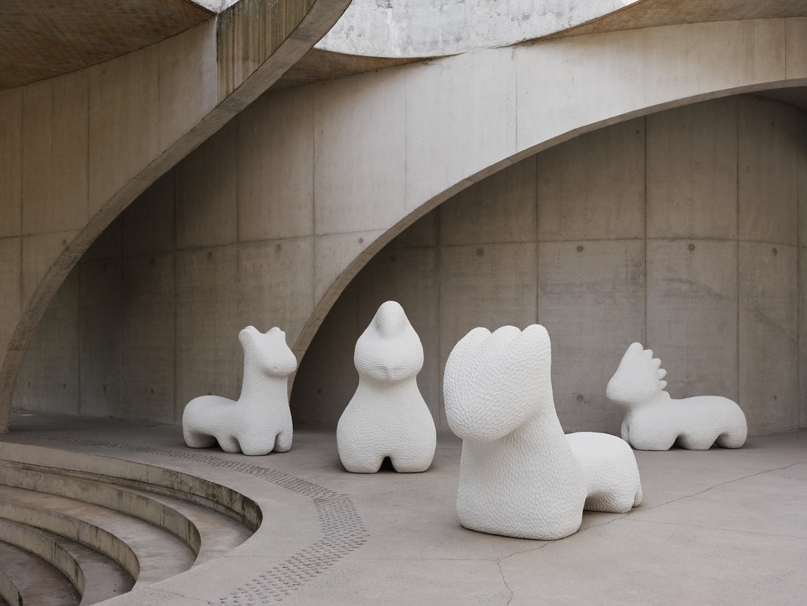 Modern art sculptures of abstract white figures in a concrete architectural setting with curved walls and steps.