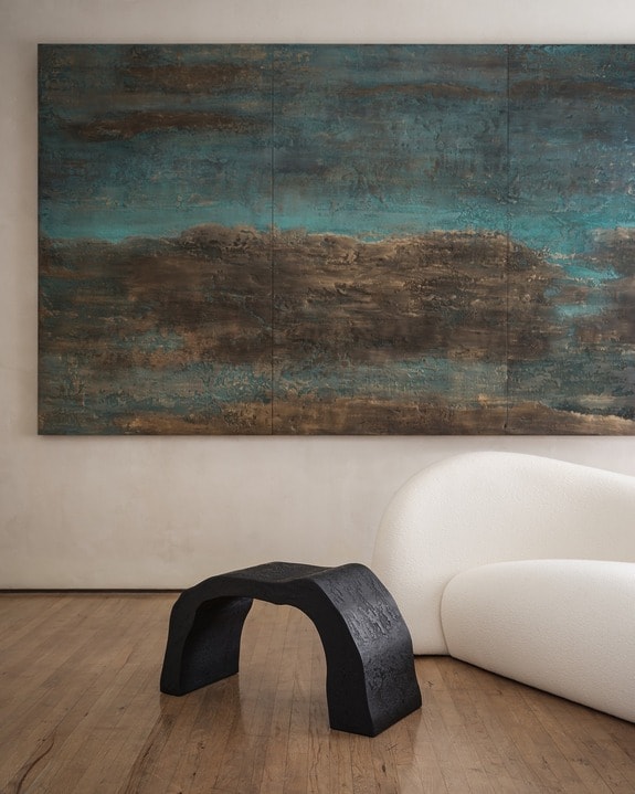 Modern artwork on wall above curved white sofa and unique black sculptural coffee table on wooden floor.