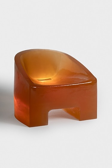 Orange modern sculptural chair with a glossy finish against a plain white background.
