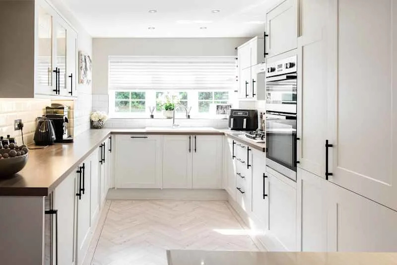 A general interior view of a new white fitted kitchen with black handles