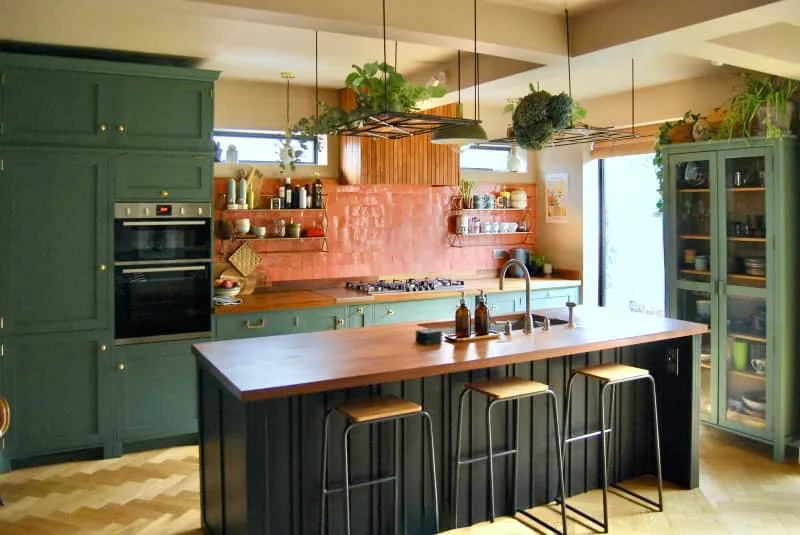 Kitchen with large wooden island with green cabinets and terracotta backsplash.