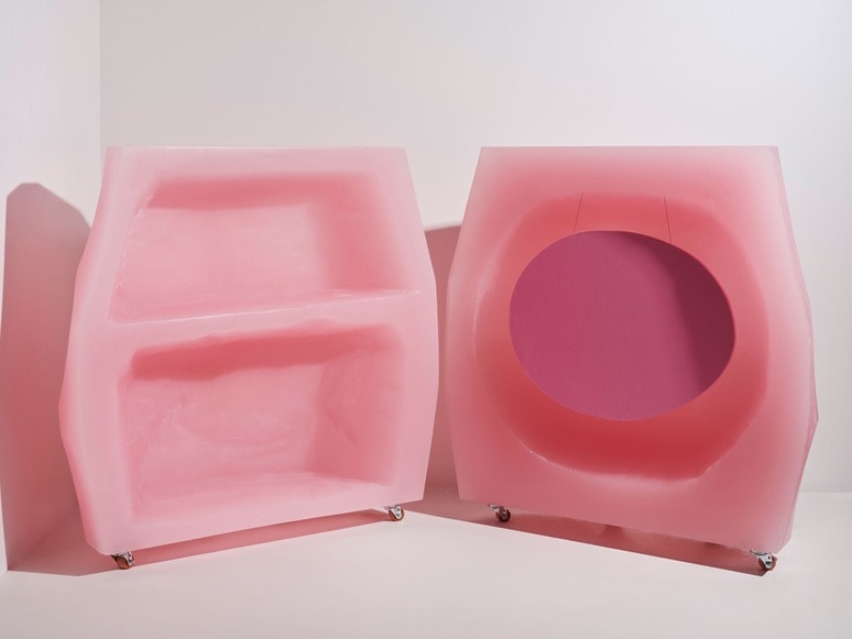 Two pink abstract geometric sculptures with smooth surfaces, one with shelves and the other with a circular opening.