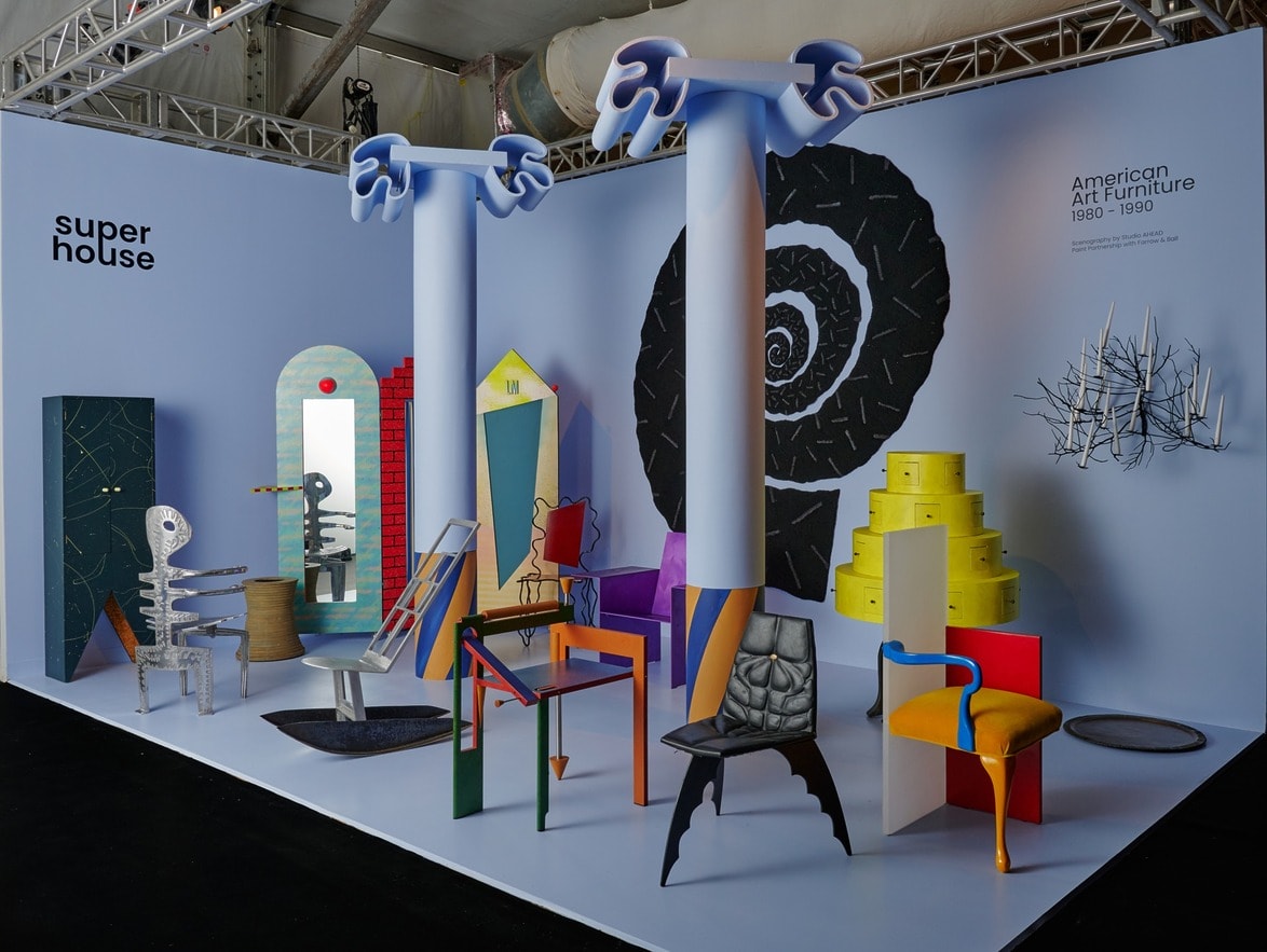 Exhibition of colorful, abstract furniture from 1980-1990 on a stage with a blue background and modern lighting.